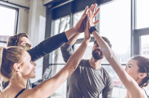 Happy young athletic people in sportswear giving high five in gym